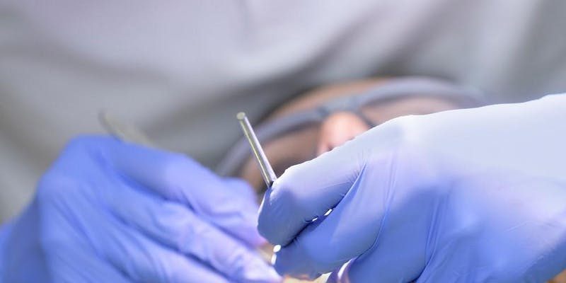 Photograph of a dentist's gloved hands working in a patient's mouth performing and oral exam